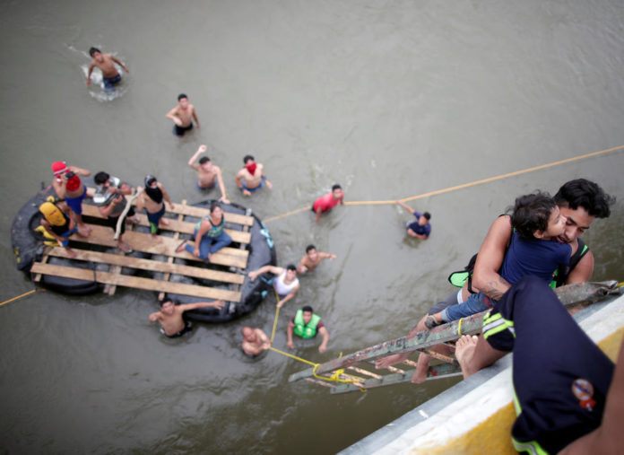 Central American migrants, part of a caravan trying to reach the U.S., use a provisional ladder to climb down from the bridge that connects Mexico and Guatemala